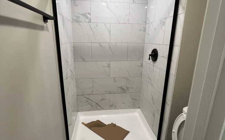 Modern walk in shower with white marble tiles and black sliding glass door frame