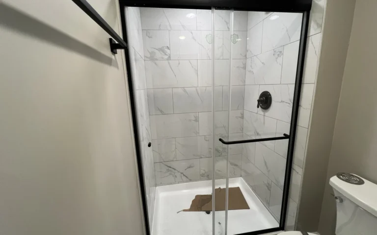 Modern walk in shower with white marble tile and black frame sliding doors