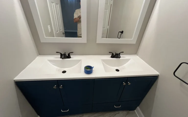 Navy blue double bathroom vanity with white countertop and black faucets during caulking
