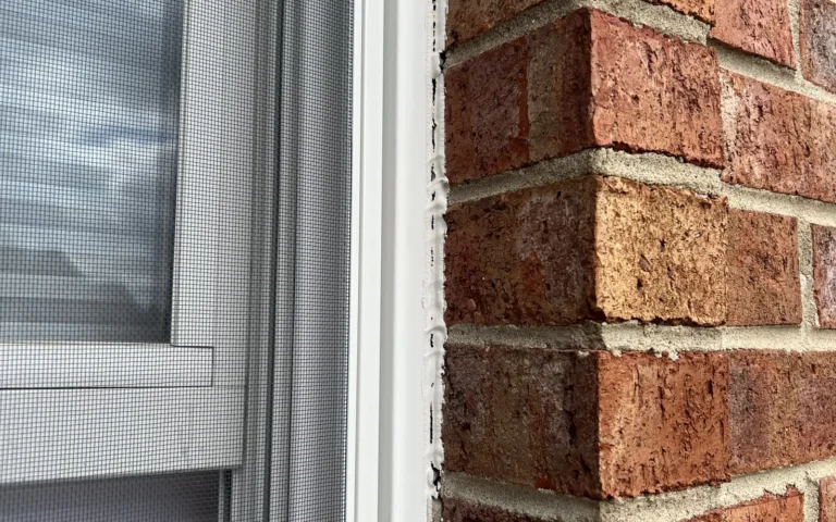 White caulk applied to seal the gap between a window frame and red brick wall