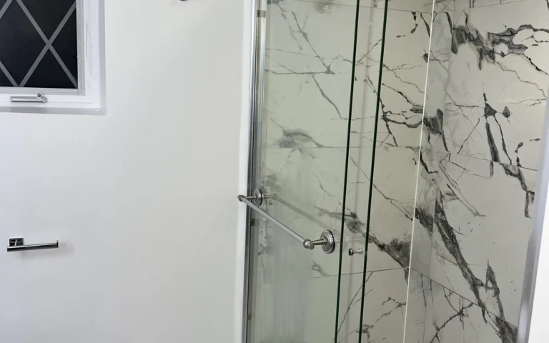 Finished bathroom shower with marble look tiles and glass sliding doors