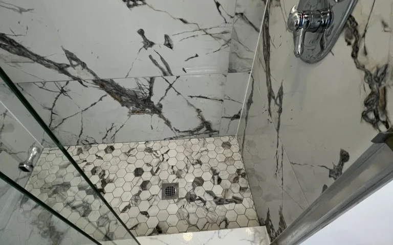 Finished walk in shower with white marble wall tiles and hexagonal floor mosaic