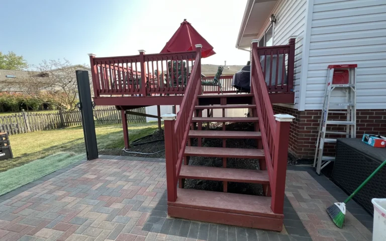 Red wooden deck with stairs and white post caps attached to a house exterior