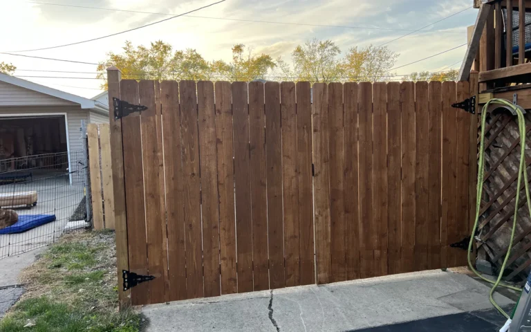 Newly installed stained wooden double fence gate with black hinges next to a deck