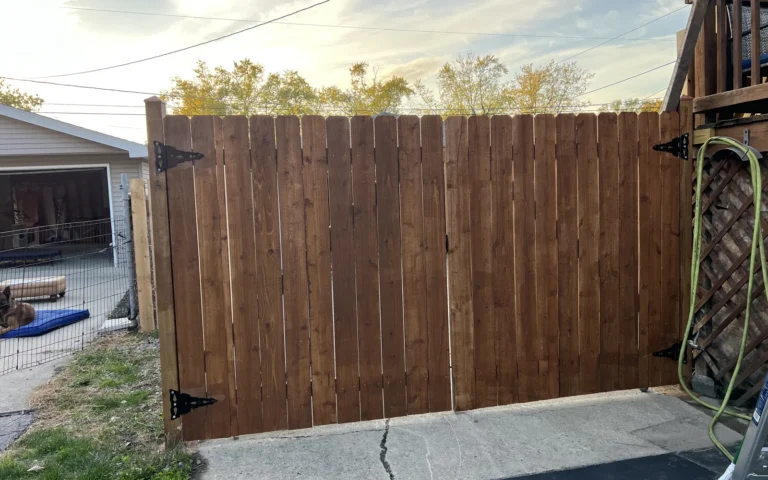 Newly installed wooden privacy fence and gate with black hinges in a residential backyard