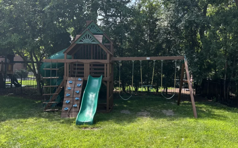Wooden backyard playground set with green slide and swings on a lawn