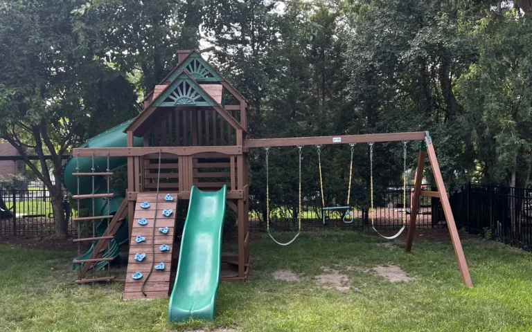 Wooden backyard playground set with green slides and swing set in a grassy yard