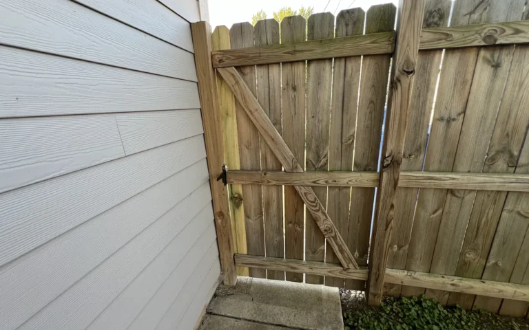 Repaired wooden privacy gate with diagonal brace and latch next to house siding