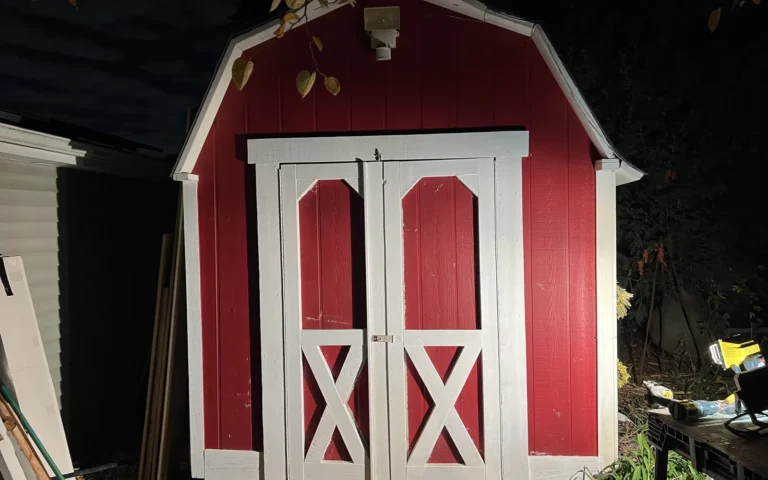 Red shed with white barn style double doors and X bracing installed at night