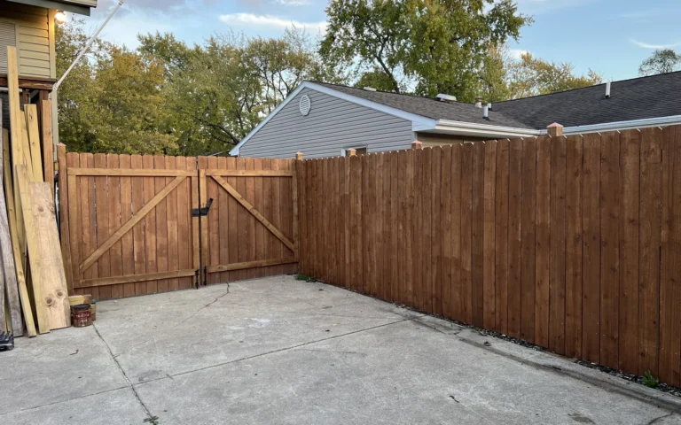 New wooden privacy fence and double gate installation with stained wood and concrete driveway