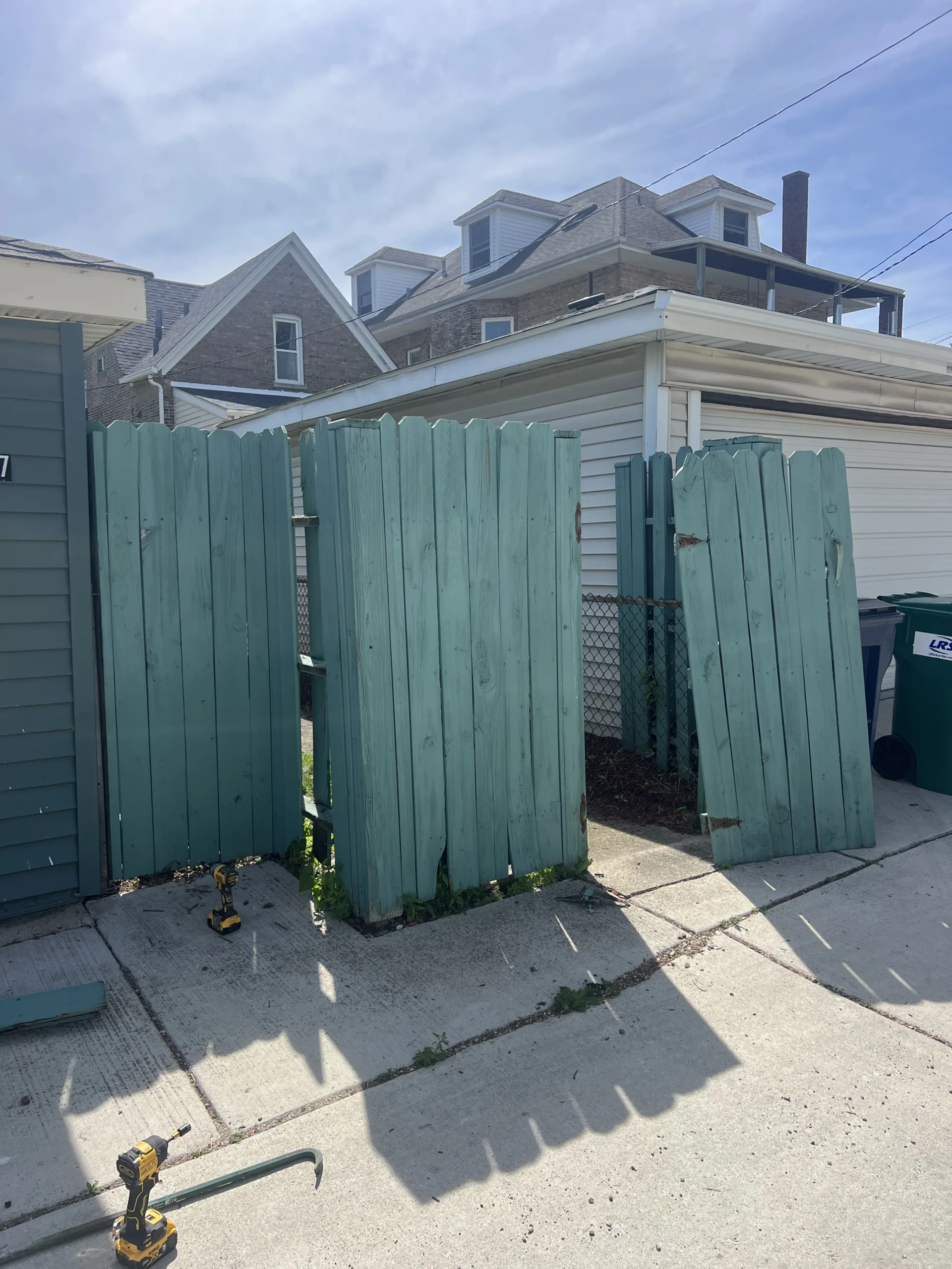 Old green wood fence panels before repair near garage and driveway in Chicago