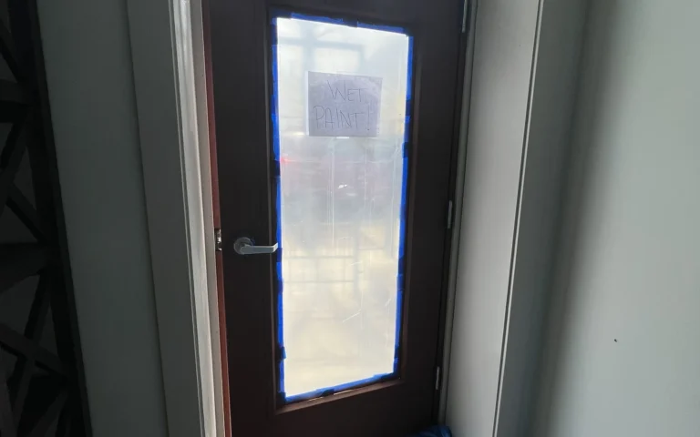 Freshly painted entry door with glass pane blue painters tape and wet paint sign