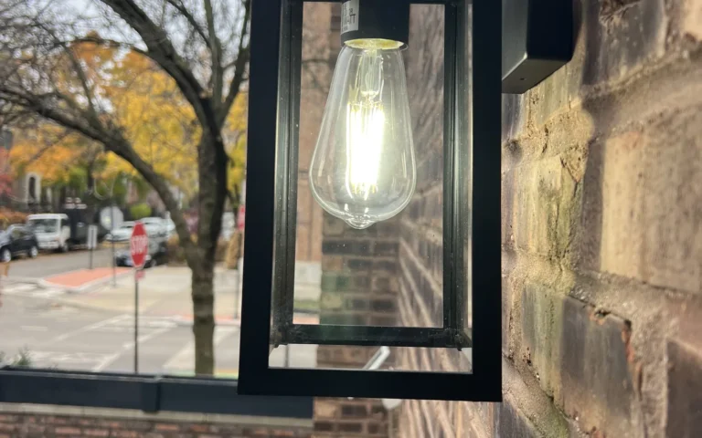 Black outdoor lantern light fixture mounted on brick wall with glowing Edison bulb