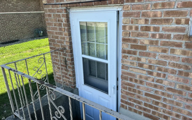 White storm door installation on brick exterior wall with metal railing