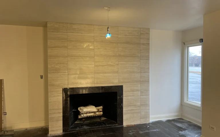 Renovated fireplace with beige stone tile surround and dark interior hearth in a room under renovation