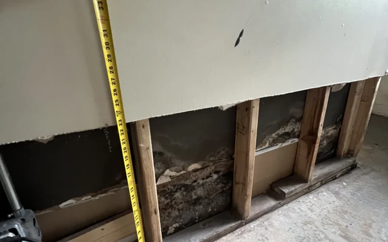 Handyman measuring exposed basement wall studs for drywall repair estimate