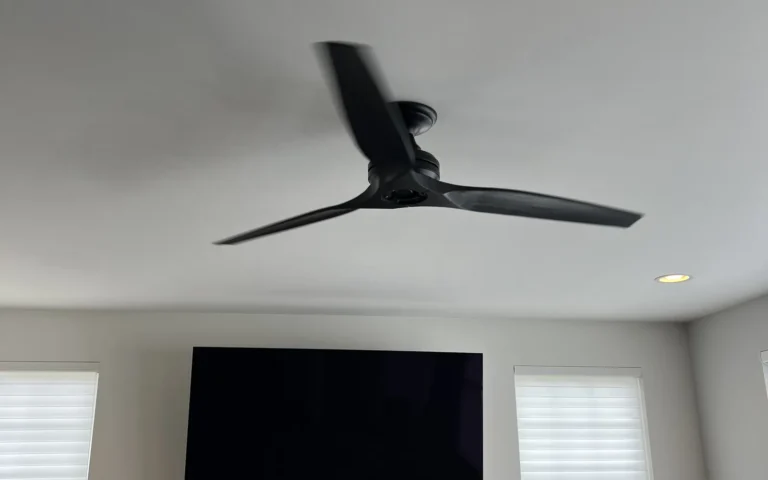 Black ceiling fan installed in living room above fireplace and TV with ladder nearby