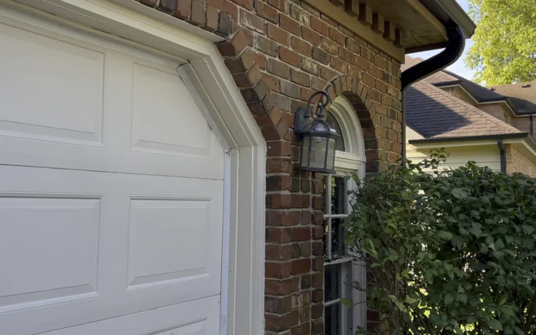 Black outdoor lantern light fixture installed on brick wall near white garage door