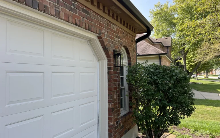 Black outdoor lantern light fixture installed on brick wall next to garage door