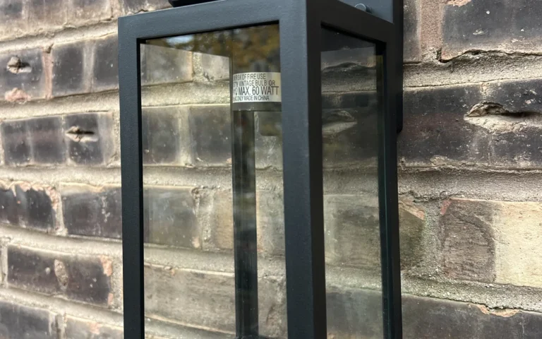 Black outdoor lantern light fixture mounted on brick wall with laser level on top