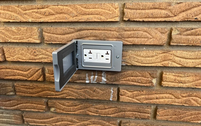 New outdoor GFCI electrical outlet with weatherproof cover installed on brick wall