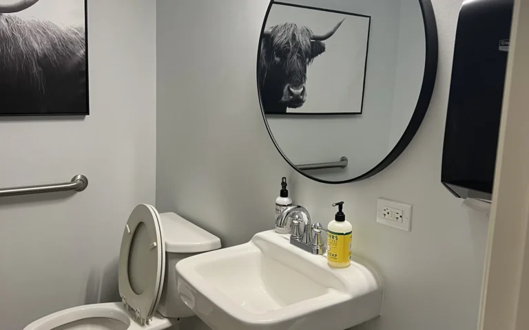 Modern bathroom renovation with white fixtures round mirror and brown tiled flooring